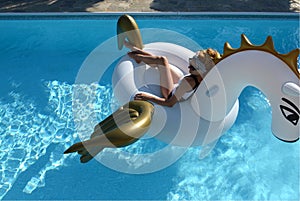 woman relaxing in luxury swimming pool resort hotel on big inflatable unicorn floating pegasus float