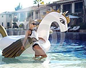 woman relaxing in luxury swimming pool resort hotel on big inflatable unicorn floating pegasus float