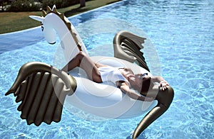 Woman relaxing in luxury swimming pool resort hotel on big inflatable unicorn floating pegasus float