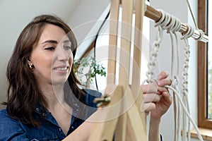 Woman relaxing and making macrame at home with different knots on a sunny day at home in attic. Stay at home hobbies