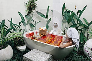 Woman relaxing in outdoor bath with flowers in Bali spa hotel