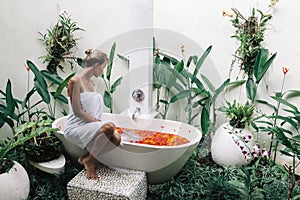 Woman relaxing in outdoor bath with flowers in Bali spa hotel