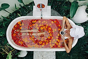 Woman relaxing in outdoor bath with flowers in Bali spa hotel