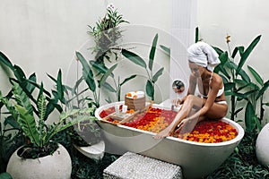 Woman relaxing in outdoor bath with flowers in Bali spa hotel