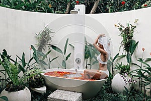 Woman relaxing in outdoor bath with flowers in Bali spa hotel