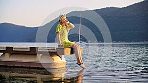 Woman relaxing on pier and touching sea water with feet