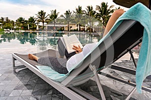 Woman relaxing and reading book on bench at swimming pool