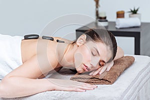 Woman relaxing and receiving hot stone massage in spa salon