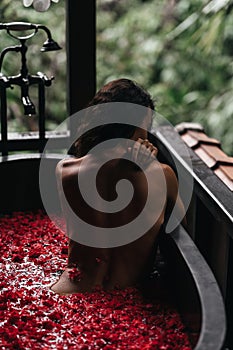 Woman relaxing in round outdoor bath with tropical flowers, organic skin care, luxury spa hotel,