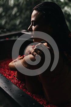 Woman relaxing in round outdoor bath with tropical flowers, organic skin care, luxury spa hotel,