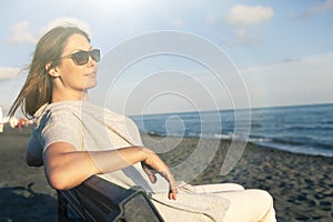 Woman relaxing at the sea dressed in peace sitting on the bench on the beach. Sunglasses