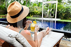 Woman relaxing sitting in desk chair near swimming pool drinking healthy pineapple juice in summer holidays.Copy space.