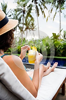 Woman relaxing sitting in desk chair near swimming pool drinking healthy pineapple juice during summer holidays.Vertical