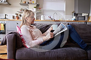 Woman Relaxing On Sofa Reading Newspaper In Modern Apartment