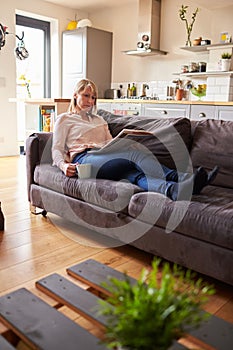 Woman Relaxing On Sofa Reading Newspaper In Modern Apartment