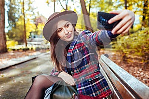 Woman relaxing in spring park. Girl taking selfie on smartphone sitting on bench outdoors
