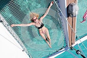 Woman relaxing on a summer sailing cruise,lying in hammock of luxury catamaran near picture perfect white sandy beach on