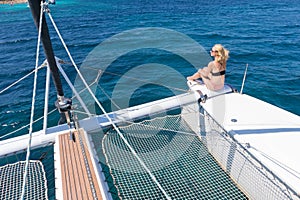 Woman relaxing on a summer sailing cruise, sitting on a luxury catamaran near picture perfect white sandy beach on