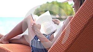 Woman, relaxing on sunbed and reading book, beach and swimwear for summer vacation. Nature, resting and enjoying holiday