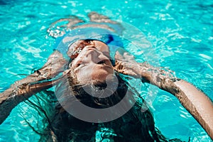 Woman relaxing swimming pool. Happy woman in a blue swimsuit floating in the pool, look form above
