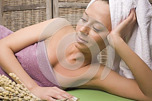 Woman relaxing on towel in stylish wooden bathroom with flowers, organic skin care, luxury spa hotel, lifestyle photo