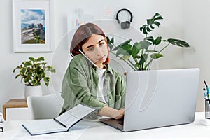 Woman remotely working at home with laptop computer. Young businesswoman talking by phone. Concept of online business or