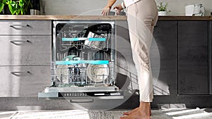 A woman removes clean ceramic dishes from dishwasher. Household and useful technology concept.