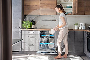 A woman removes clean ceramic dishes from the dishwasher. Household and useful technology concept.