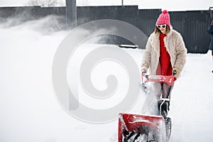 Woman removes snow from pathway with a snow thrower machine