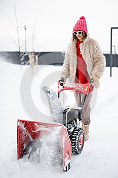 Woman removes snow from pathway with a snow thrower machine