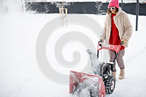 Woman removes snow from pathway with a snow thrower machine