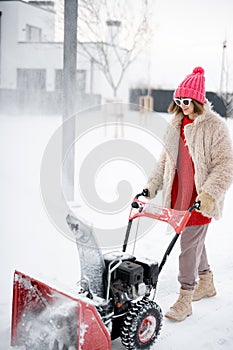 Woman removes snow from pathway with a snow thrower machine