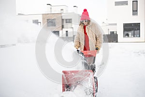 Woman removes snow with a snow thrower machine near house