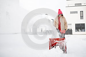 Woman removes snow with a snow thrower machine near house