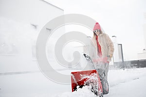 Woman removes snow with a snow thrower machine near house