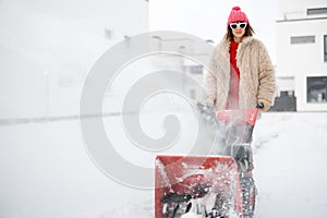 Woman removes snow with a snow thrower machine near house