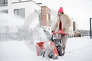 Woman removes snow with a snow thrower machine near house