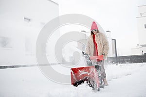 Woman removes snow with a snow thrower machine near house