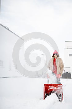 Woman removes snow with a snow thrower machine near house