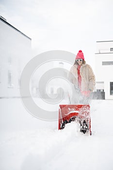 Woman removes snow with a snow thrower machine near house