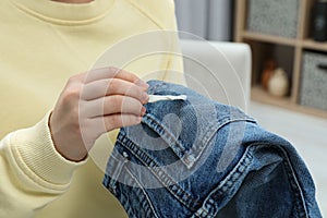 Woman removing chewing gum from jeans indoors, closeup