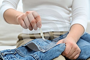 Woman removing chewing gum from jeans on sofa, closeup