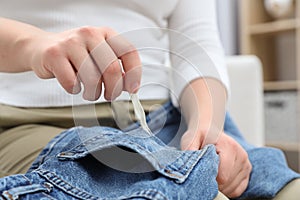 Woman removing chewing gum from jeans on sofa indoors, closeup