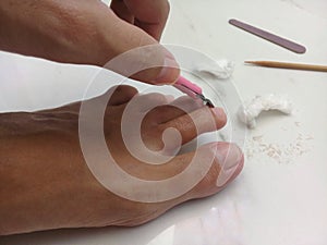 Woman removing cuticles from toes with pliers at home photo