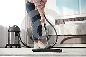 Woman removing dirt from carpet with vacuum cleaner at home