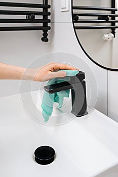 Woman removing dirt and scale from water tap in bathroom photo