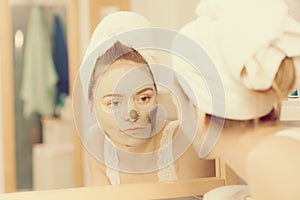 Woman removing facial clay mud mask in bathroom