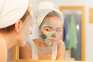 Woman removing facial clay mud mask in bathroom