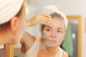 Woman removing facial clay mud mask in bathroom