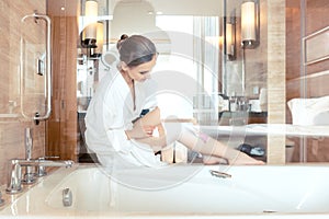 Woman removing hair by shaving her legs in bathroom of hotel photo